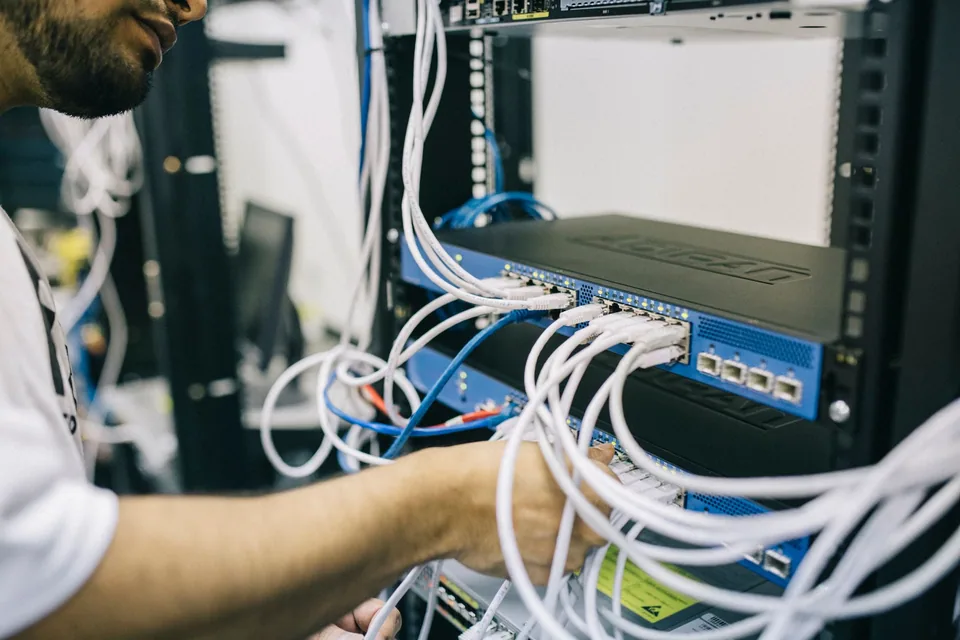 Técnico organizando cabos de rede em rack com switch e patch panel